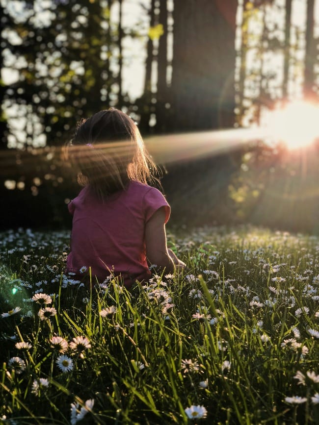 My family was enjoying some time on a hike in a wooded area. The way the light was coming through the trees and across the grass and daisies was making me itch to capture the moment.
I got down on my stomach in the grass to capture this photo of my daughter Ellie. All I had with me that day was my iPhone X which was still a champ for captuing the moment perfectly. I just love the way the end of the day sunlight was making her glow. To me this photo perfectly captures summer, childhood, and my sweet girl, who shines brighter then the sun.